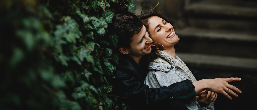 Young couple hugging sit near greenery wall and laughing